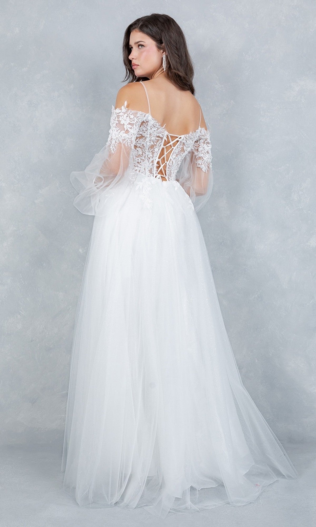 A woman wearing the Cinderella Couture 4234 long formal dress, featuring a white off-the-shoulder lace and tulle design with elegant lace appliqué and a corset bodice, stands against a light gray textured background, facing away from the camera.